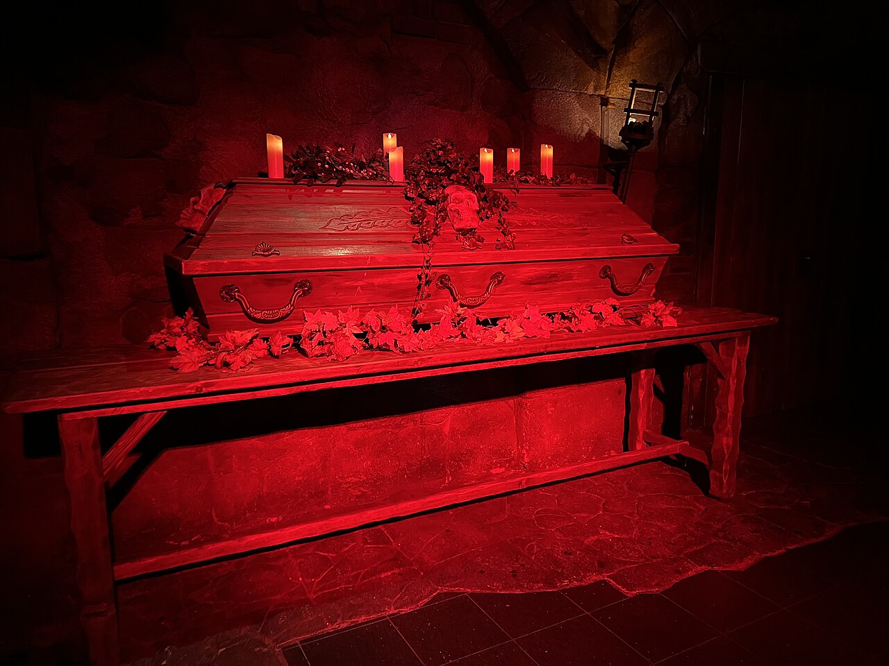 Ein Holzsarg mit Kerzen und Rosen auf einem Tisch, in rotes Licht getaucht