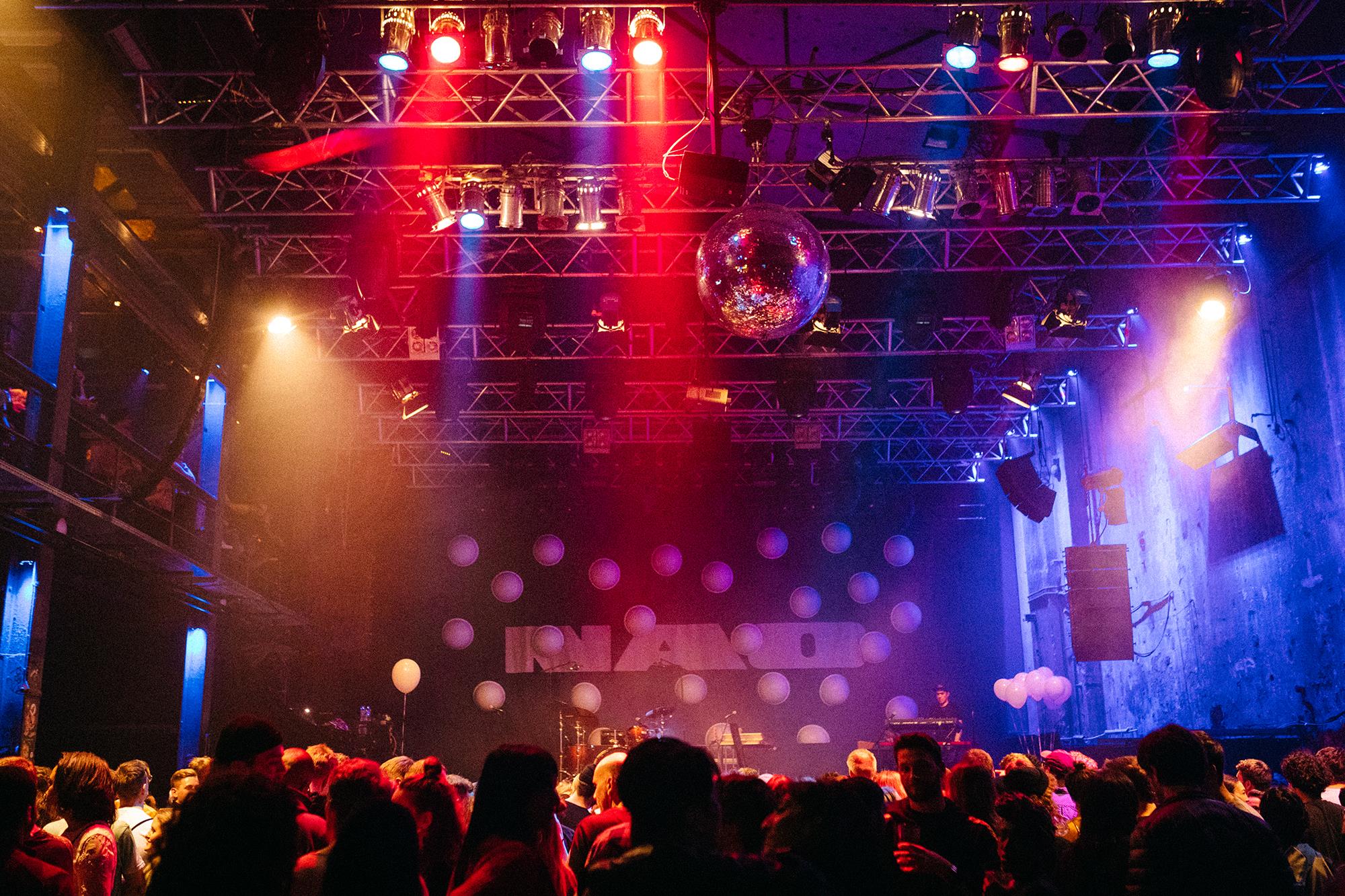 Eine volle Tanzfläche in einem Clubsaal unter Scheinwerfern, buntem Licht und einer Discokugel