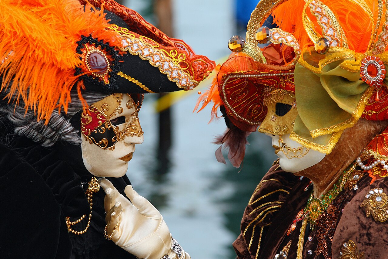 Zwei Menschen in prachtvollen venezianischen Kostümen mit weißen Masken und Federhüten, einander zugewandt