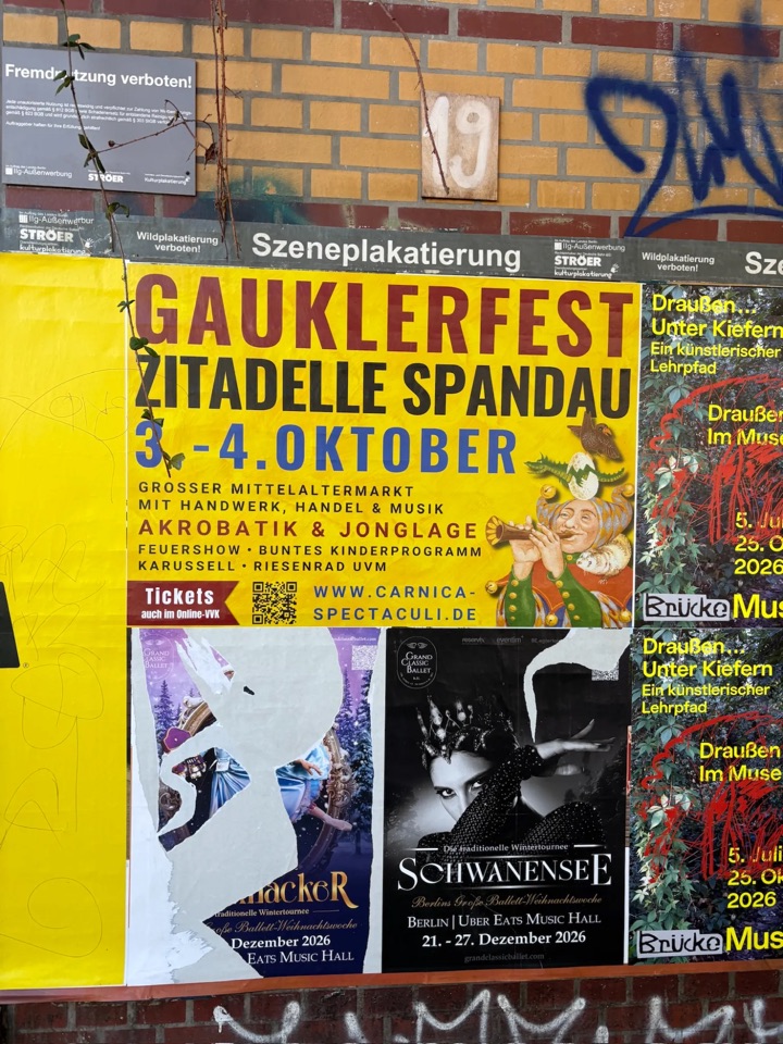 Plakatwand an einer Backsteinmauer mit Plakaten für das Gauklerfest in der Zitadelle Spandau und für Schwanensee