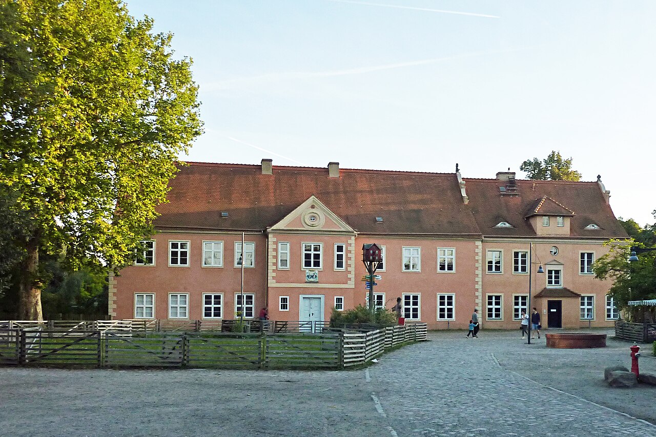 Das rosafarbene Gutshaus der Domäne Dahlem mit Hof und Bäumen an einem Sommertag