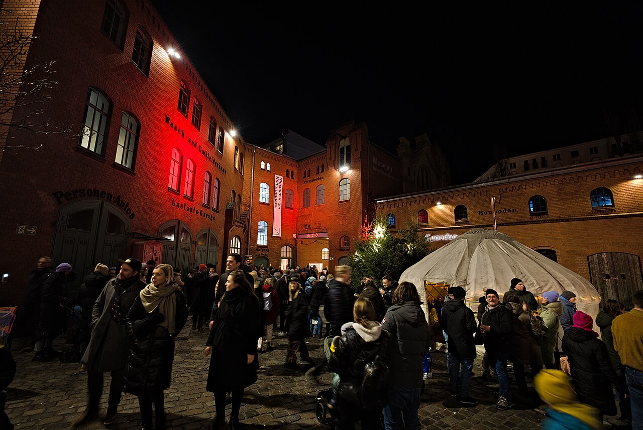 Besucher im Hof der Kulturbrauerei zwischen beleuchteten roten Backsteingebäuden und einem weißen Zelt