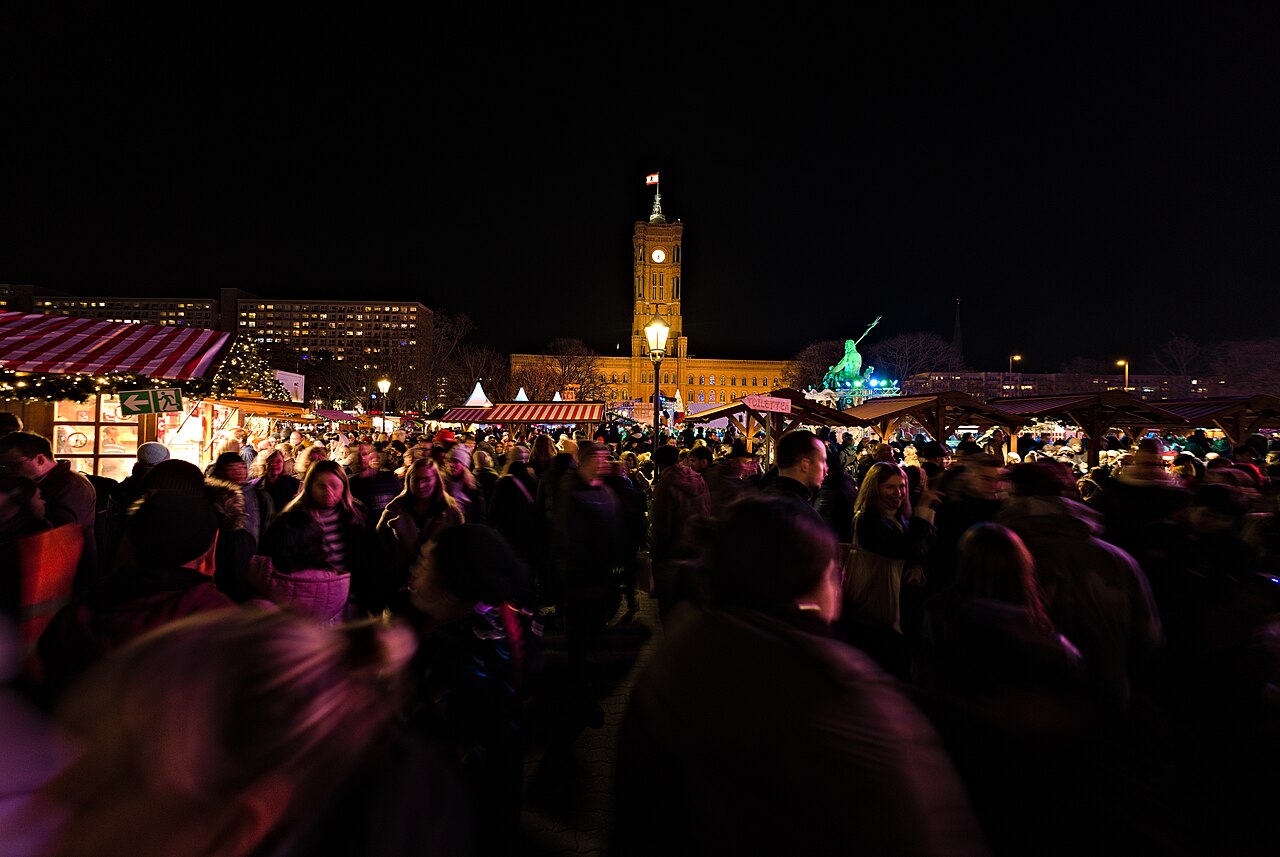 Dichtes Gedränge zwischen Marktständen bei Nacht, im Hintergrund der beleuchtete Turm des Roten Rathauses