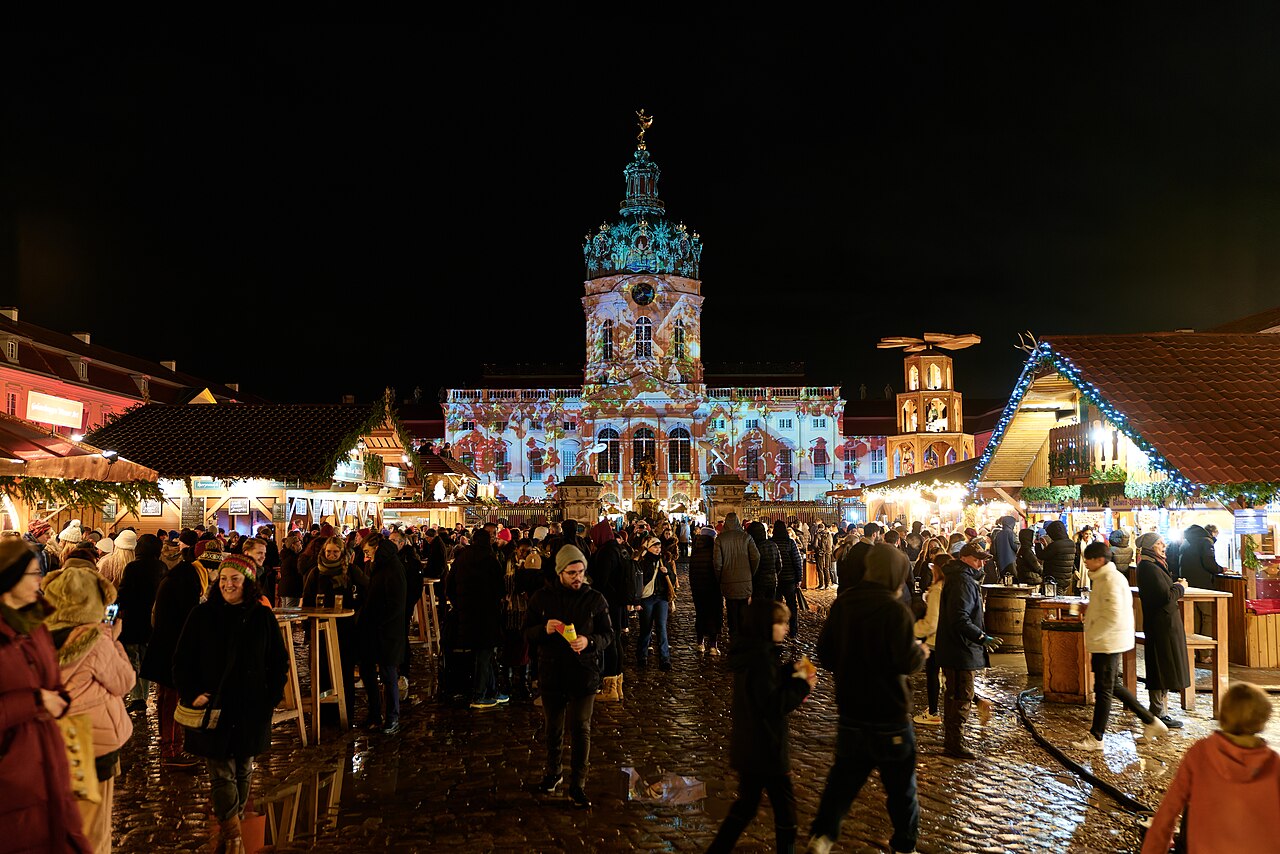 Das bunt angestrahlte Schloss Charlottenburg hinter Marktständen und dichtem Publikum